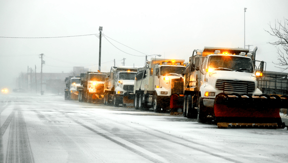 A line of snow fighting trucks on an icy road